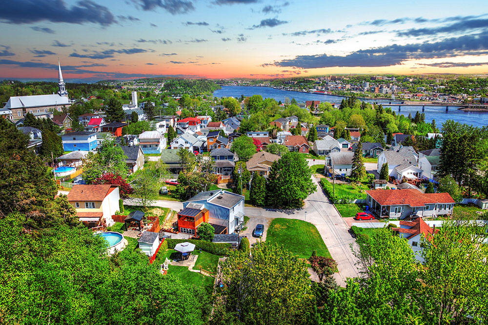Vue aérienne du Saguenay–Lac-Saint-Jean, mettant en avant des maisons et la verdure, illustrant l'accessibilité des services de télémédecine de la Clinique Omicron pour les résidents de la région.