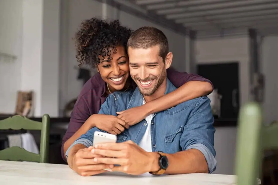 Couple smiling and interacting with a smartphone in a cozy indoor setting, reflecting the accessible healthcare services and teleconsultation options at Clinique Omicron.
