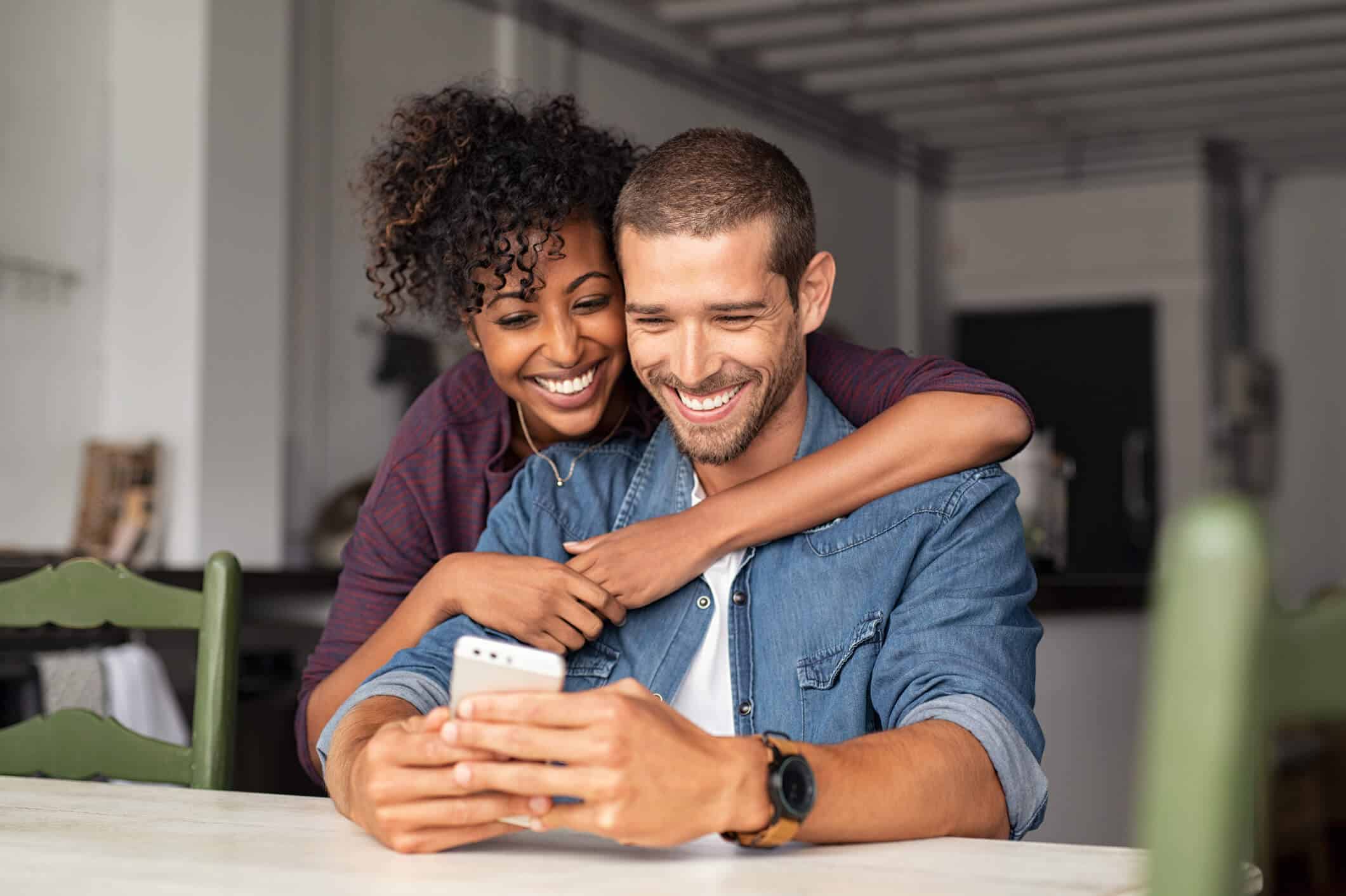Couple smiling and interacting with a smartphone in a cozy indoor setting, reflecting the accessible healthcare services and teleconsultation options at Clinique Omicron.