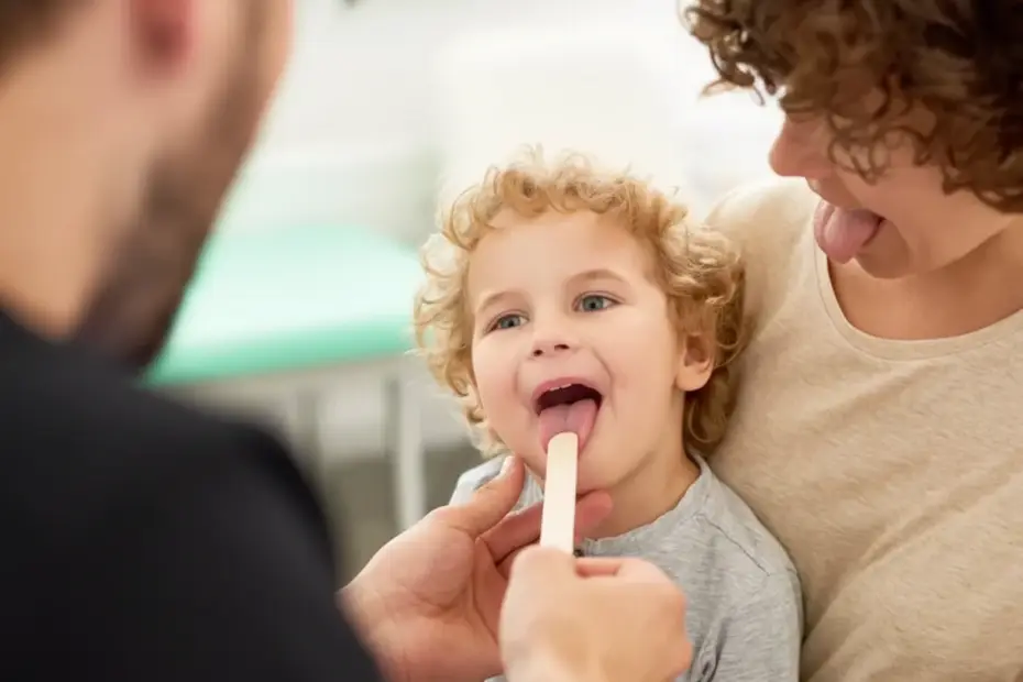 Enfant souriant pendant un examen m&eacute;dical, avec un parent tenant une spatule, dans un environnement clinique accueillant.