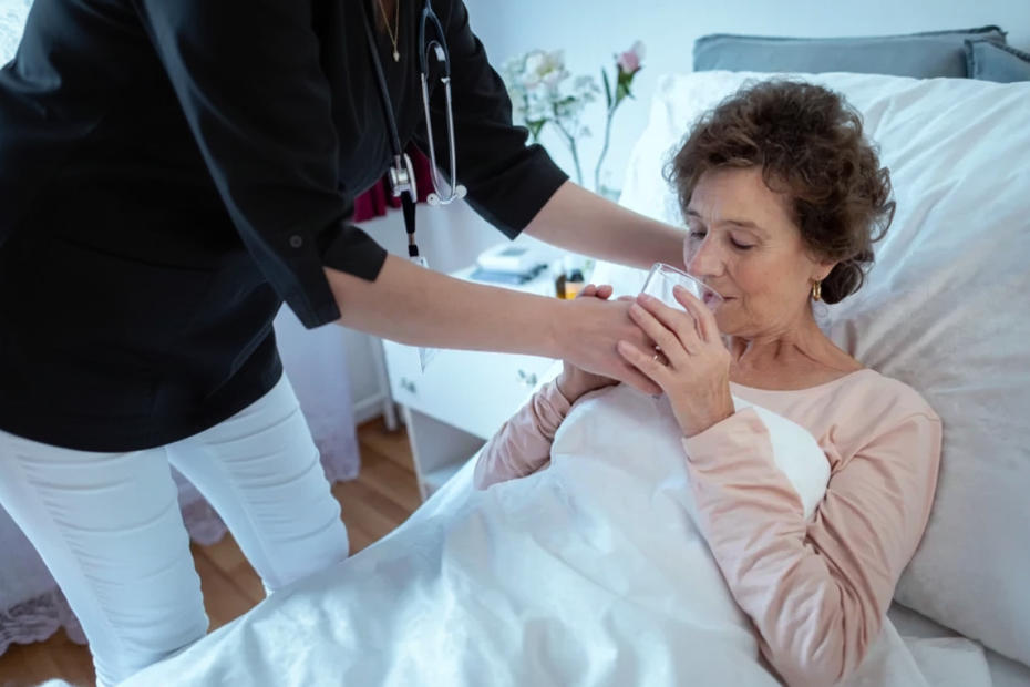 Infirmière aidant une patiente âgée à boire un verre d'eau, soins à domicile, Clinique Omicron.