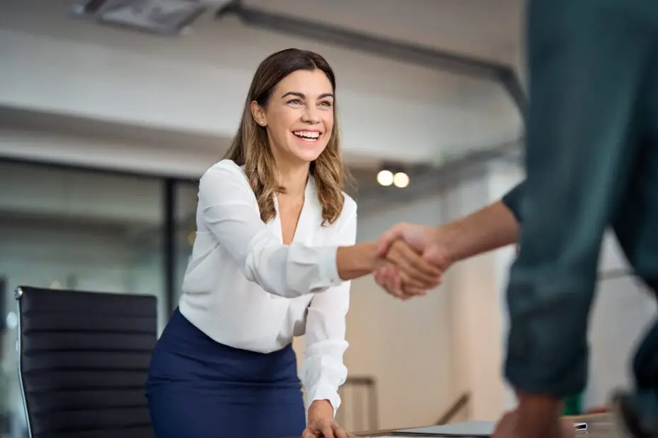 Femme souriante en chemise blanche serrant la main d'un homme, illustrant un accueil chaleureux dans un environnement professionnel, symbolisant les services de téléconsultation de santé offerts par Clinique Omicron.